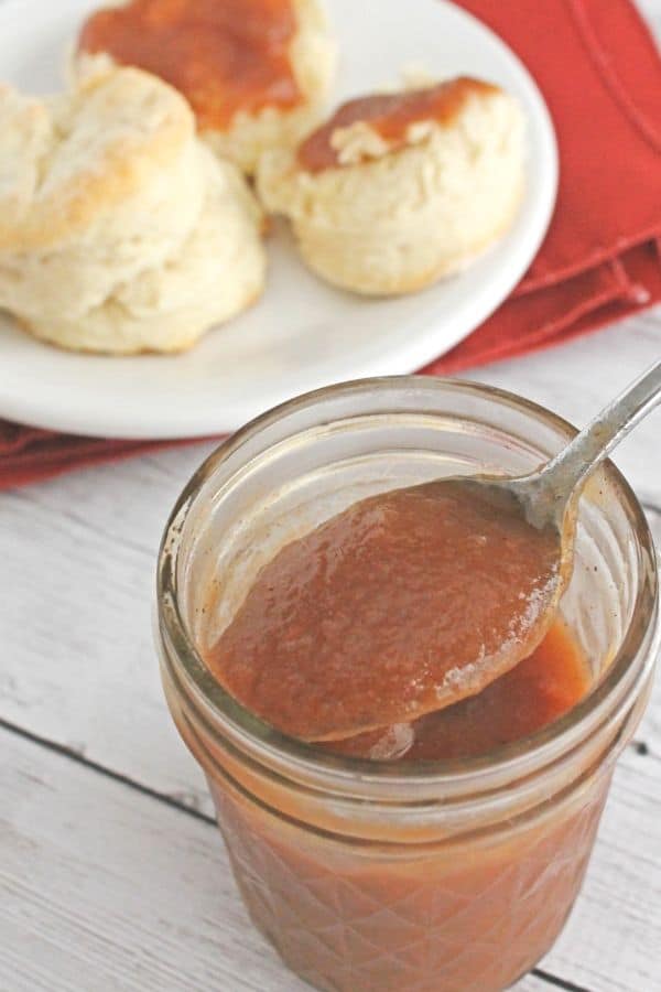 jar of slow cooker apple butter next to a plate of biscuits
