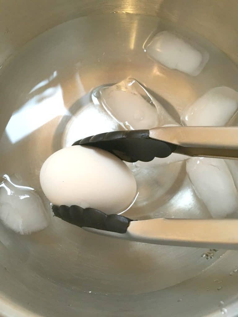 hard boiled egg being lowered into an ice bath with tongs