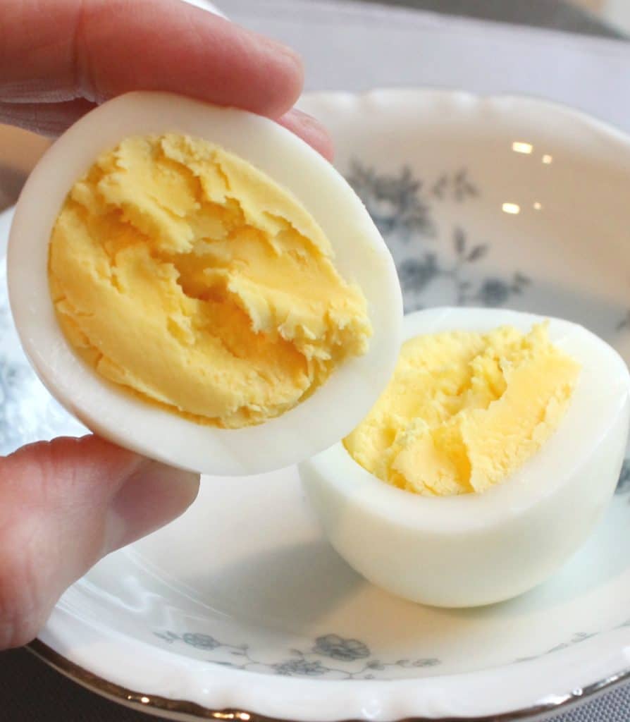 fingers holding half of a hard boiled egg, showing the perfect yolk