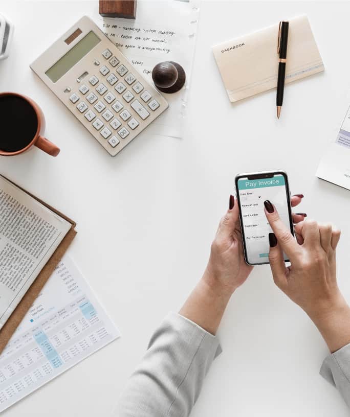 woman making calculations for paying off our debt, using a smart phone, calculator, pen and paper.