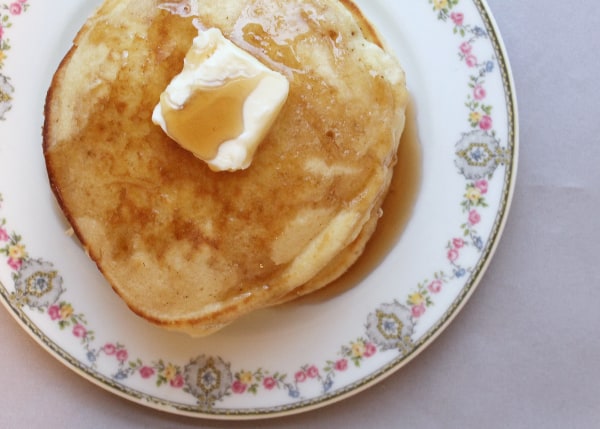 homemade fluffy pancakes on a china plate, topped with syrup and butter