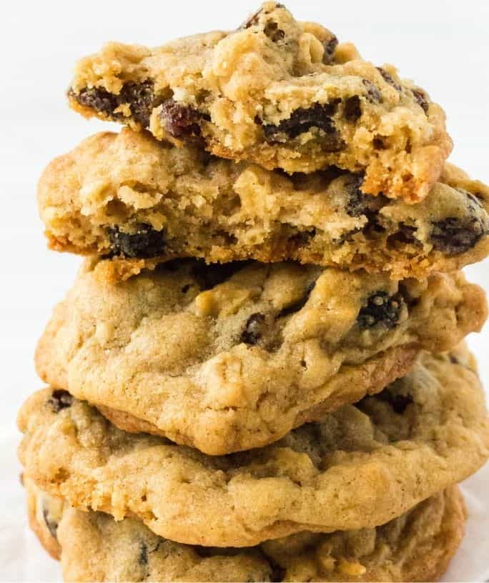 a stack of bakery style oatmeal raisin cookies, with one torn in half to show how soft and chewy it is