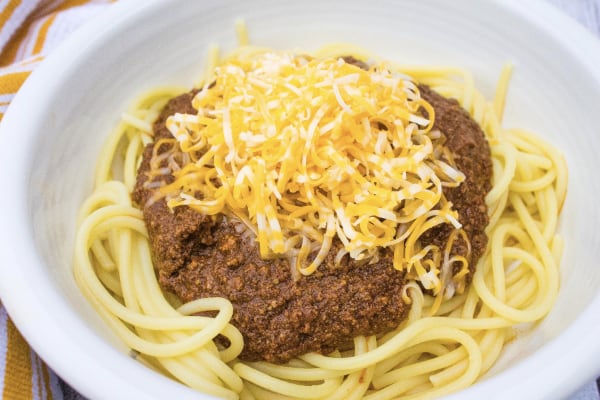 instant pot skyline chili topped with cheese and served over spaghetti in a white bowl