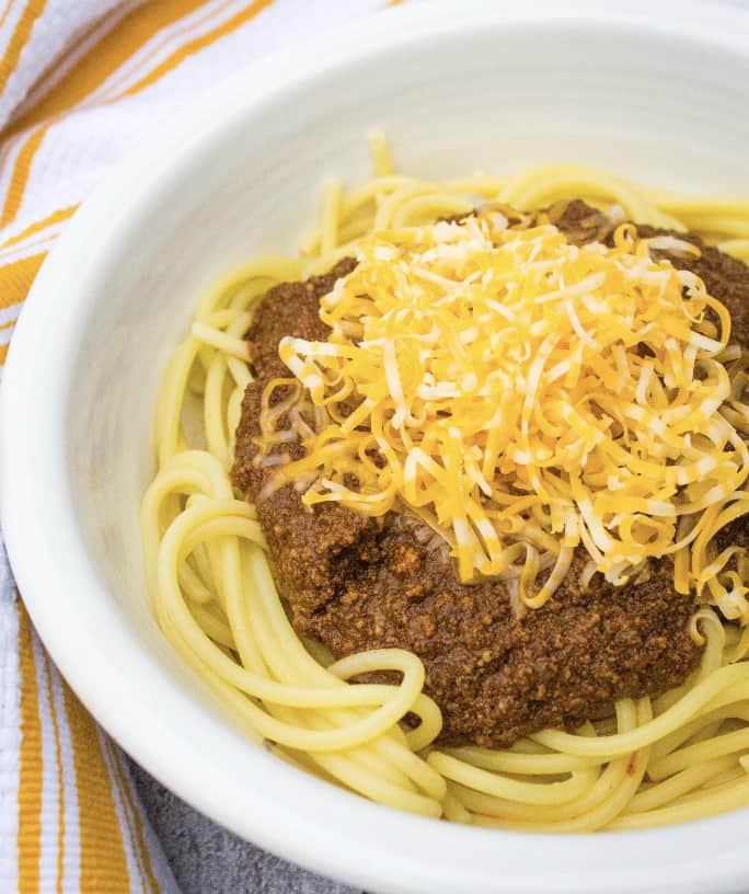 white bowl filled with spaghetti topped with Instant Pot Cincinnati Chili and shredded cheese