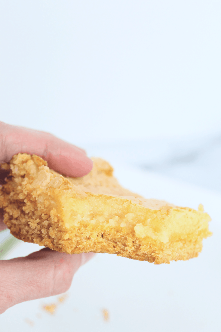 a woman's hand holding a square of ooey gooey butter cake, with a bite taken out of the square