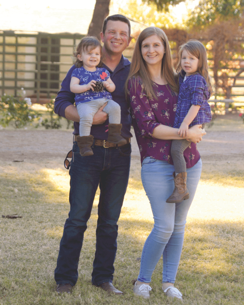 A man holding a toddler and a woman holding a preschooler. They are standing in a yard.