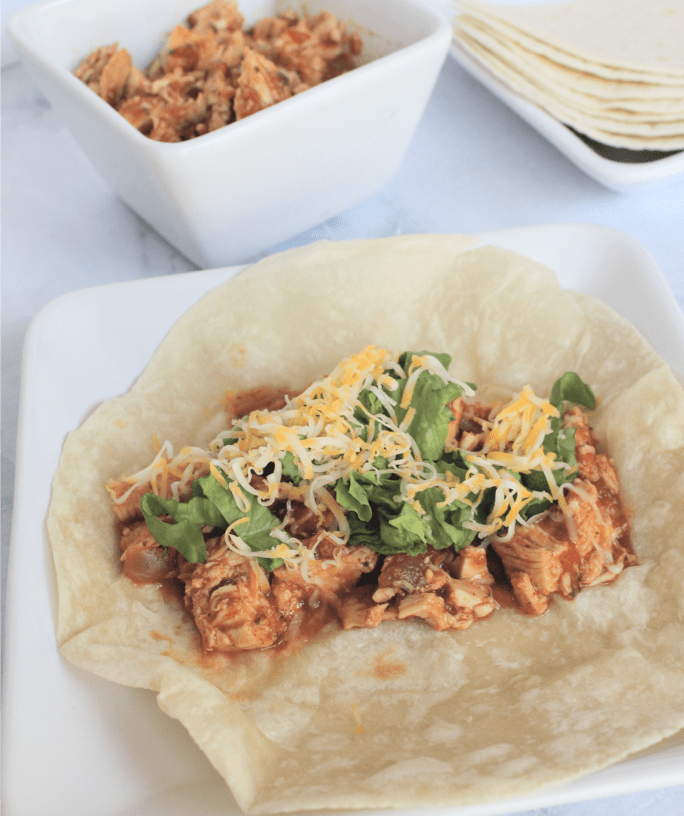 tortilla filled with taco chicken, lettuce, and cheese atop a white plate