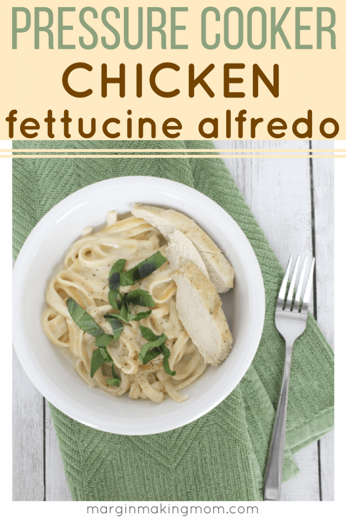 White plate with fettucine alfredo and sliced chicken breast, topped with fresh basil, all resting on a green napkin.