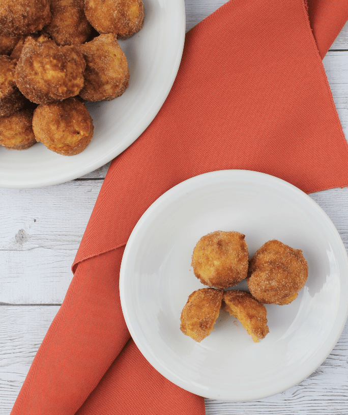 pumpkin donuts on a white plate next to an orange cloth napkin