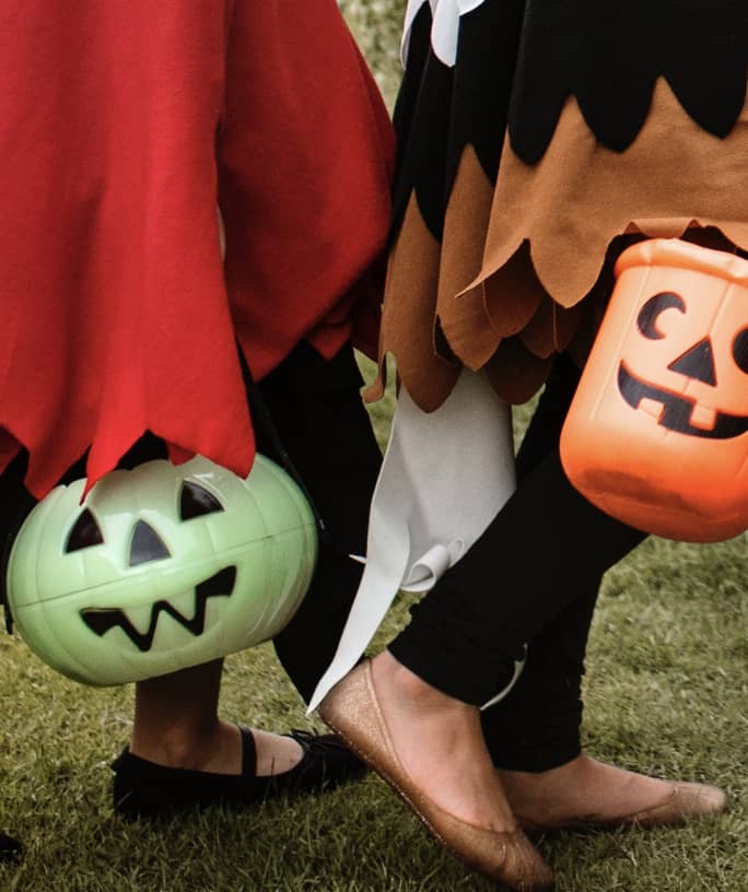 Green pumpkin bucket and orange pumpkin bucket in the hands of trick or treaters who are walking outside