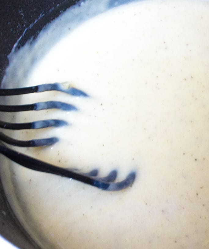 homemade cream of chicken soup being stirred by a black whisk in a nonstick pot