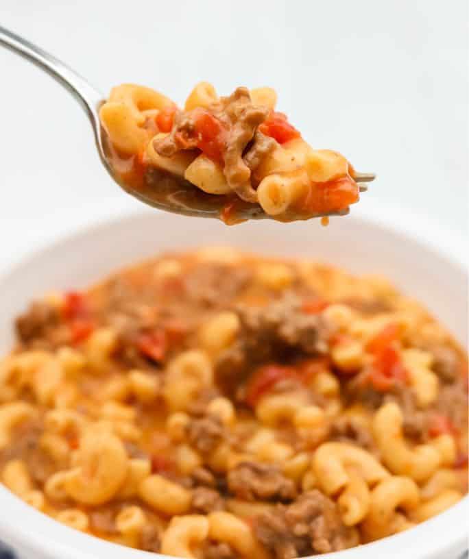 Instant Pot cheeseburger macaroni in a white bowl, with a fork lifting out a bite.