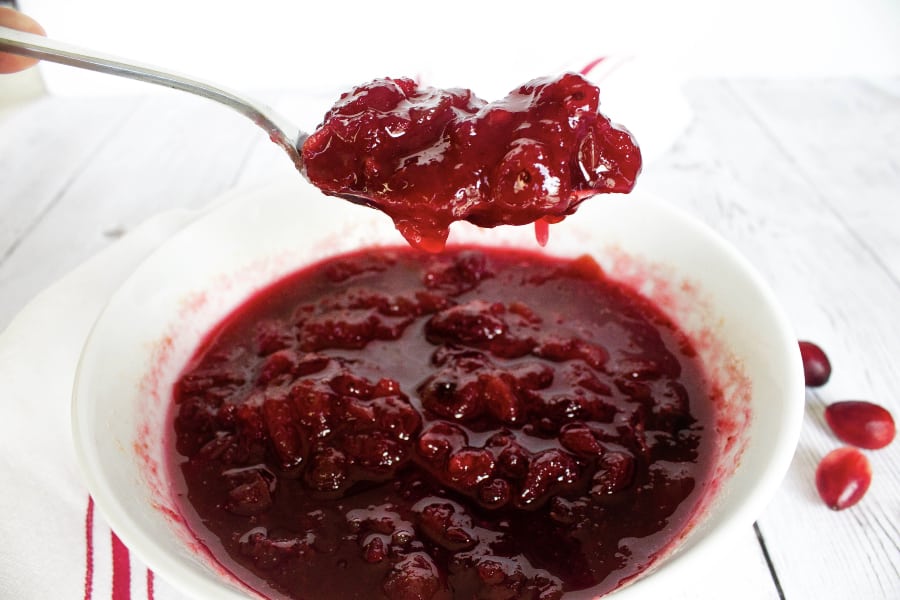 white bowl of cranberry sauce with a spoon scooping out some cranberry sauce