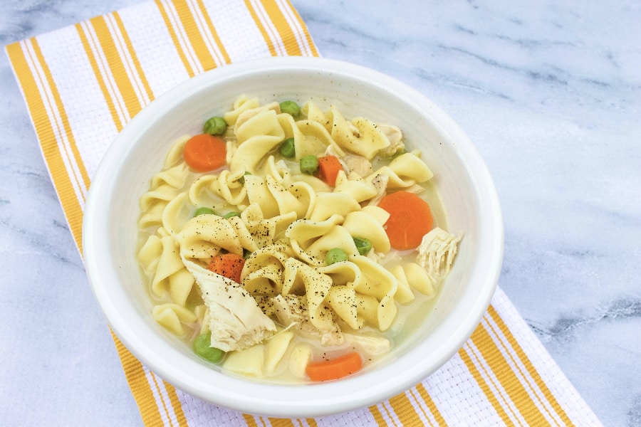 white bowl full of creamy chicken noodle soup made in the pressure cooker, resting on a white and yellow napkin