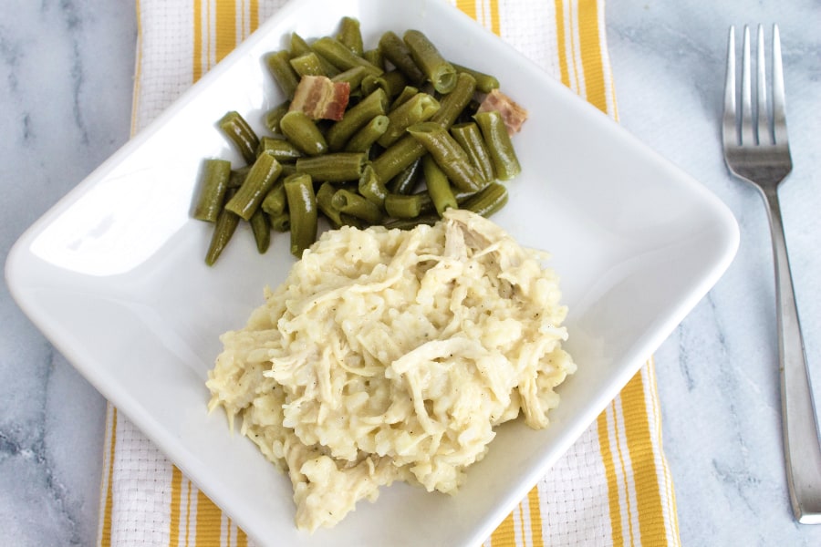 white plate with a serving of Instant Pot chicken and rice casserole along with a serving of green beans. The plate is resting on a yellow and white striped kitchen towel.