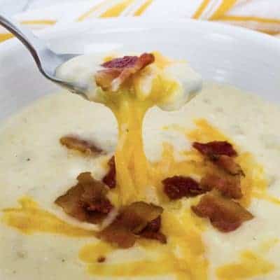 white bowl filled with instant pot potato soup, topped with bacon crumbles and melted cheese, with a spoon removing a bite of soup