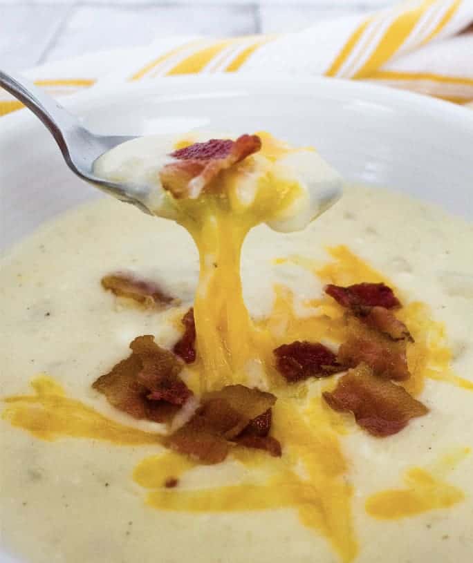 white bowl filled with instant pot potato soup, topped with bacon crumbles and melted cheese, with a spoon removing a bite of soup