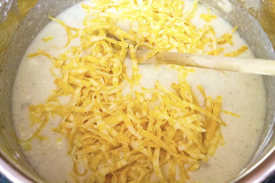 Instant Pot potato soup with shredded cheese being stirred in