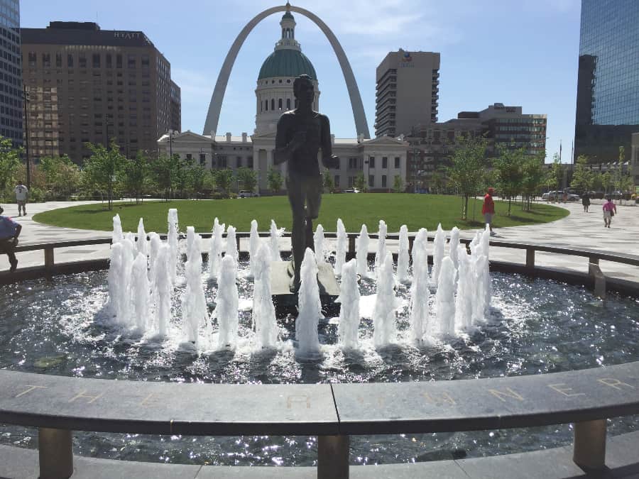 statue and fountain in front of the st louis capital and gateway arch at kiener plaza park