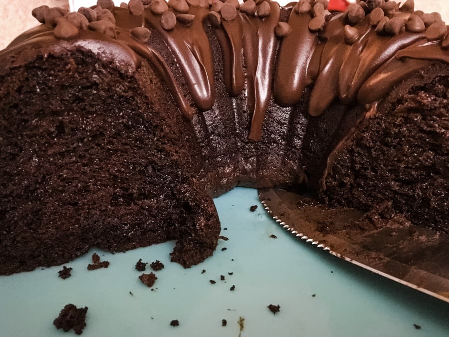 a cut chocolate bundt cake with glaze and chocolate chips on top, next to a knife