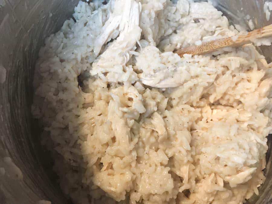 wooden spoon stirring shredded chicken, rice, and cream in an instant pot