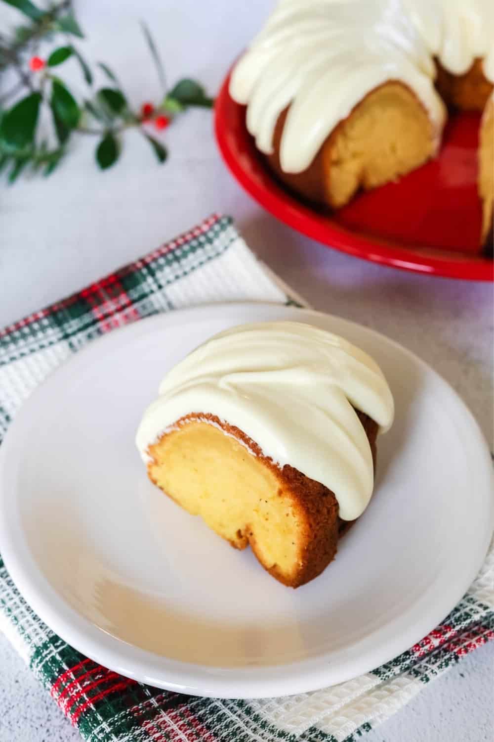a slice of the best eggnog cake made with cake mix, topped with icing and served on a white plate. The remainder of the bundt cake is in the background.