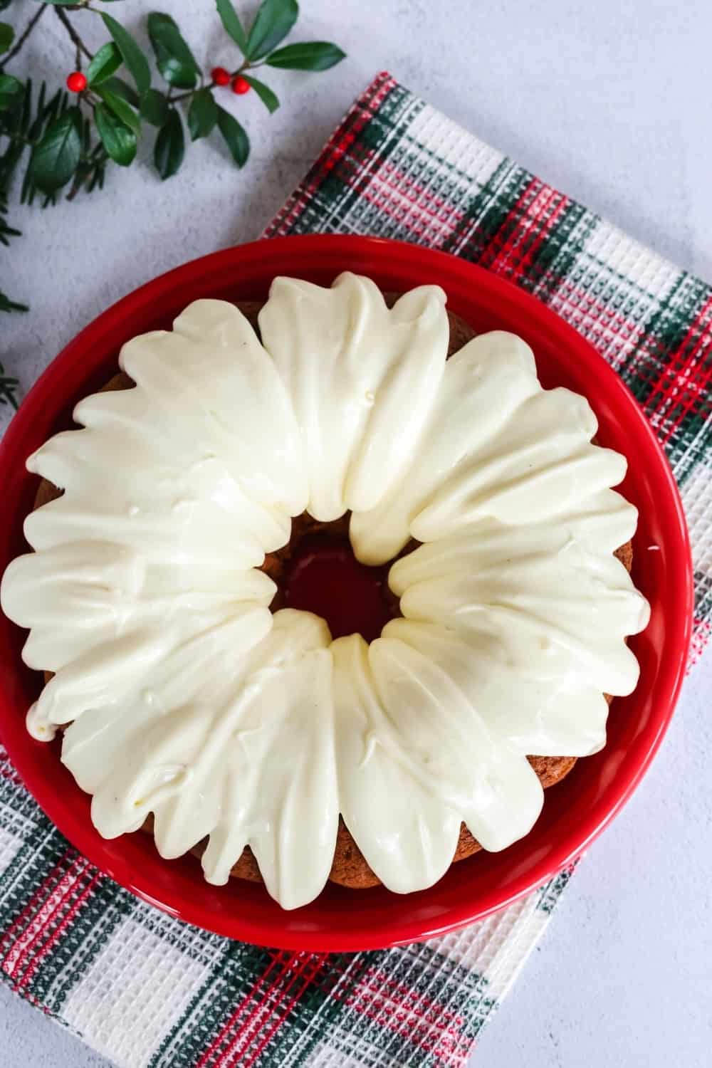 overhead view of a spiced eggnog bundt cake on a red plate, with eggnog frosting drizzled over the top of the cake.