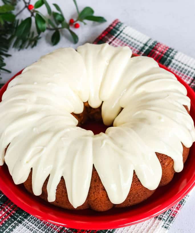 An eggnog bundt cake, made from a cake mix, is served on a red plate. It's topped with eggnog cream cheese icing.