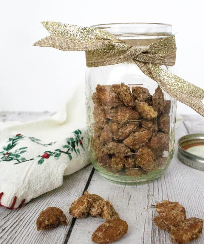 ribbon-wrapped glass jar of candied almonds next to a Christmas hand towel