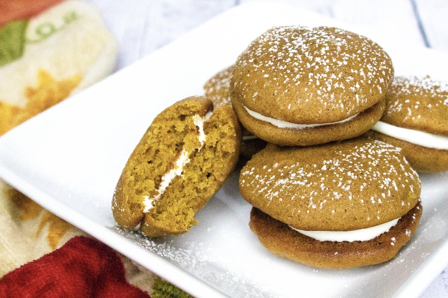 stack of pumpkin whoopie pies on a white plate, with a bite taken out of one cookie