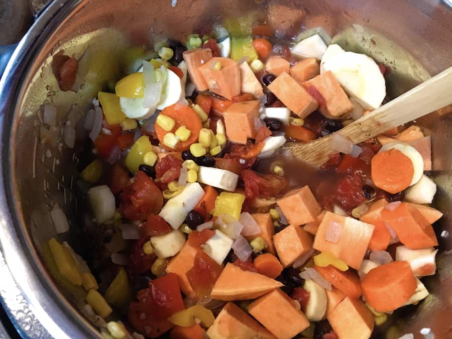 Stirring the ingredients for Sweet Potato Chili in the Instant Pot, including sweet potatoes, black beans, carrots, parsnips, onions, peppers, broth, and spices