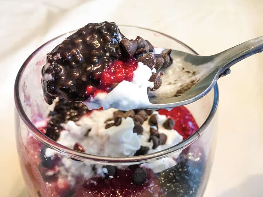 spoon scooping dark chocolate chia seed pudding with berries and cream