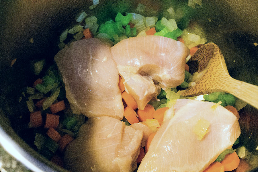 quartered chicken breast atop carrots, onions, and celery for making Instant Pot Italian Chicken Soup