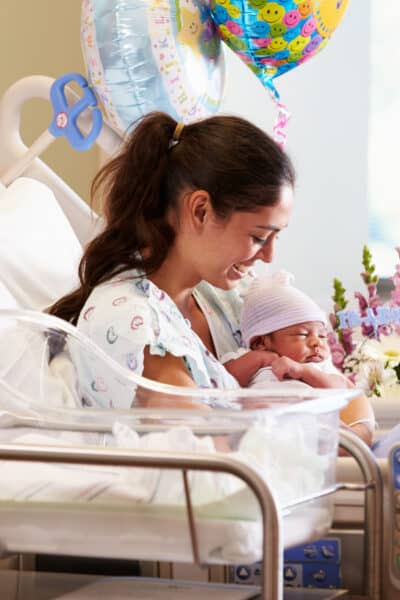 woman in a hospital's postpartum room holding her newborn baby