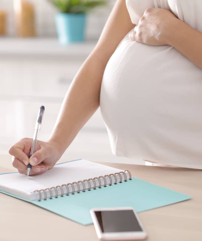 Pregnant woman writing third trimester checklist for maternity in kitchen, closeup