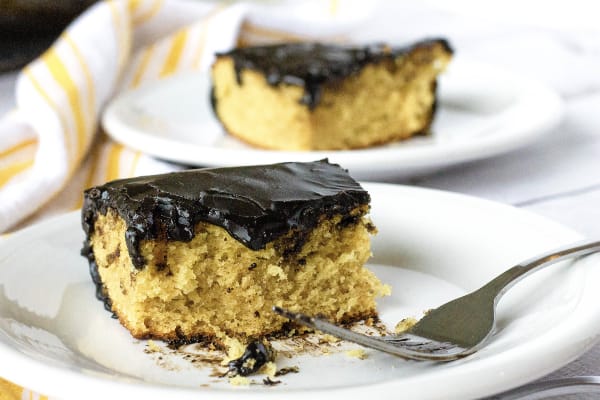 piece of peanut butter cake with chocolate frosting on a white plate, next to a fork