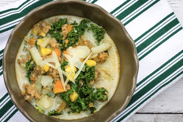 brown bowl filled with Instant Pot corn, sausage, and potato chowder; resting on a green and white striped cloth napkin