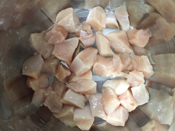 pieces of cut up chicken in the insert pot of the Instant Pot, for making Instant Pot bacon chicken ranch gnocchi