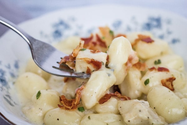 fork lifting out a bite of Instant Pot bacon chicken ranch gnocchi from a blue floral china bowl