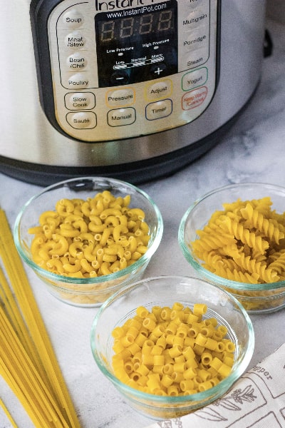 three glass bowls of dried pasta in front of an Instant Pot
