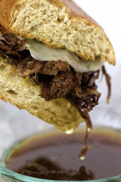 Instant Pot French Dip sandwich being dipped into a bowl of hot au jus