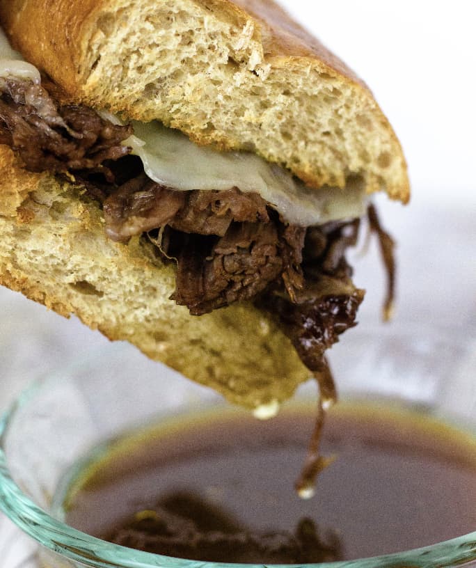 Instant Pot French Dip sandwich being dipped into a bowl of hot au jus