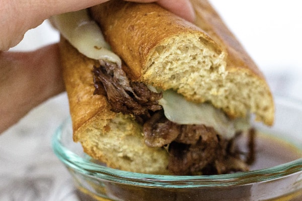 french dip sandwich being dipped into a bowl of au jus