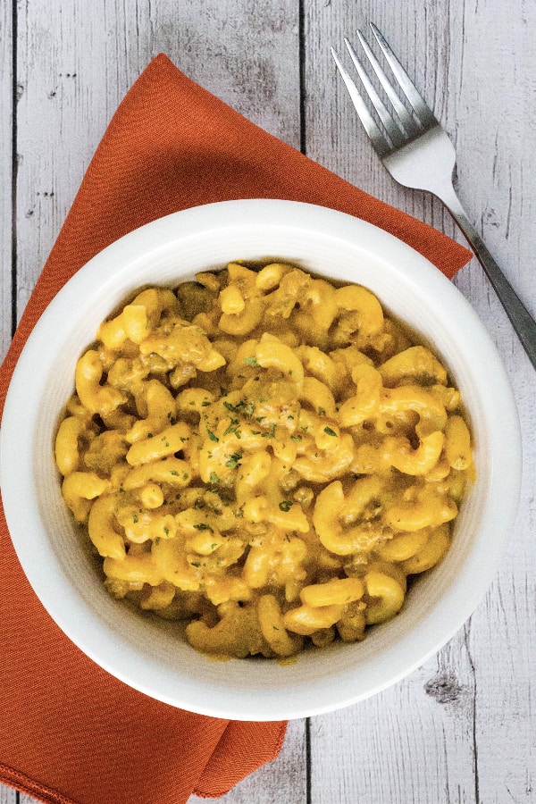 white bowl filled with Instant Pot pumpkin macaroni and cheese, resting on an orange napkin with a fork next to it