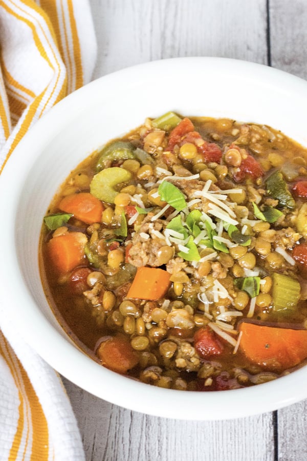 Instant Pot sausage and lentil soup in a white bowl, topped with parmesan and basil