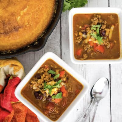 two bowls of Instant Pot pumpkin chili next to a cast iron skillet of cornbread