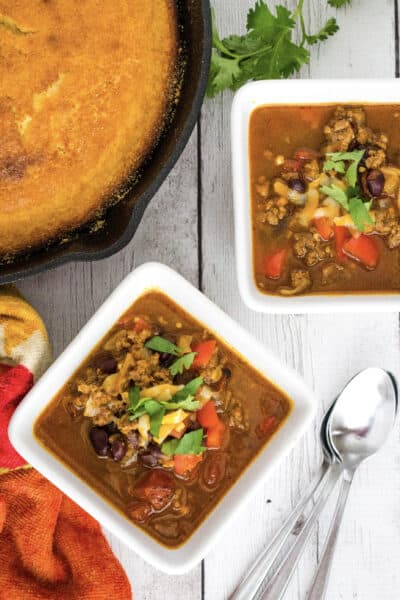 two bowls of Instant Pot pumpkin chili next to a cast iron skillet of cornbread