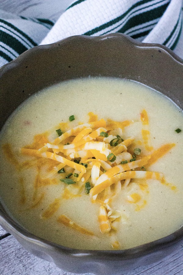 brown bowl filled with cheesy cauliflower soup, topped with shredded cheese and chives