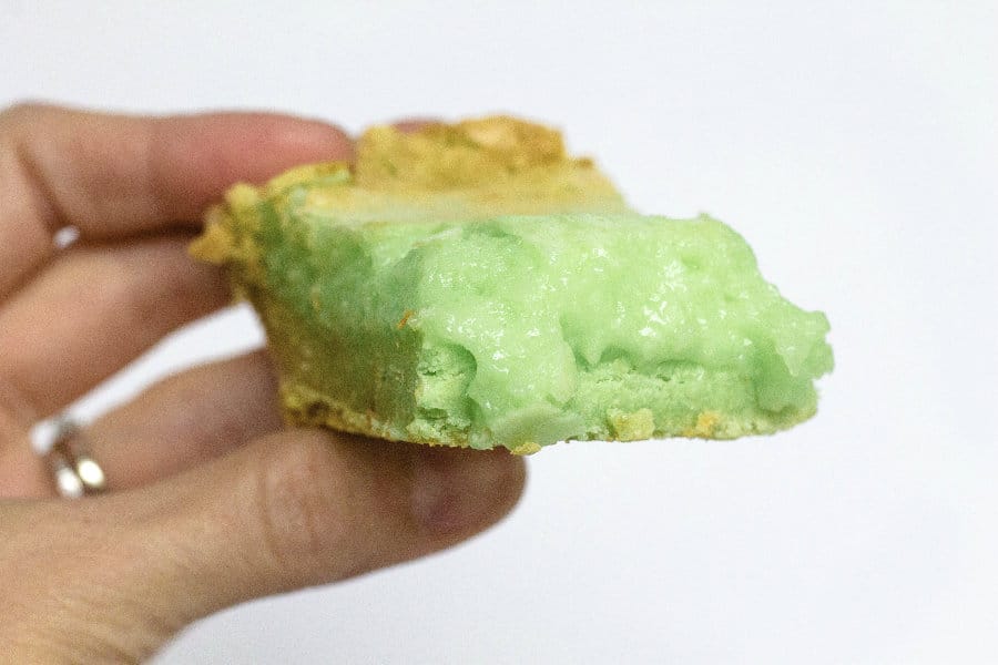 a woman's hand holding a square of pistachio ooey gooey butter cake