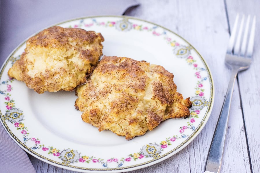 Two cinnamon sugar drop biscuits served on a China plate next to a fork